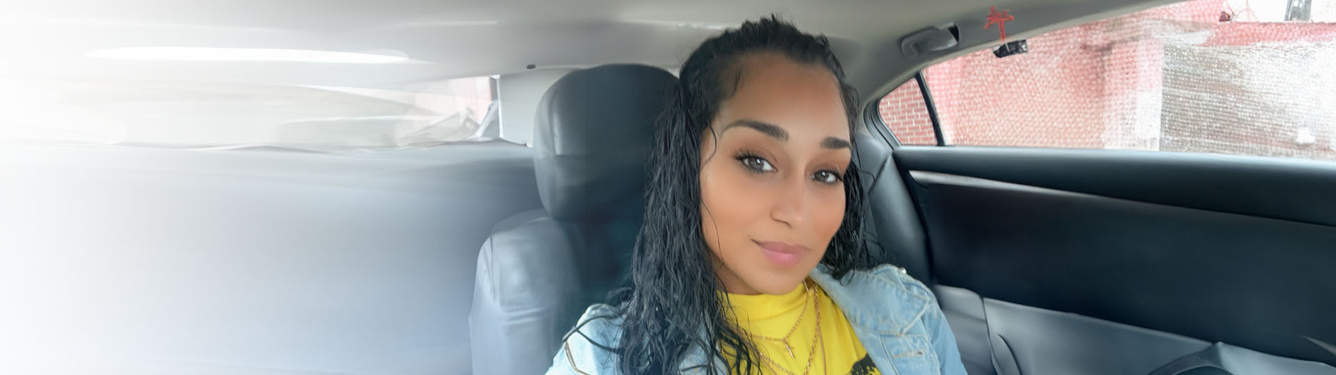 Wearing a yellow top and denim jacket while sitting in the backseat of a car.