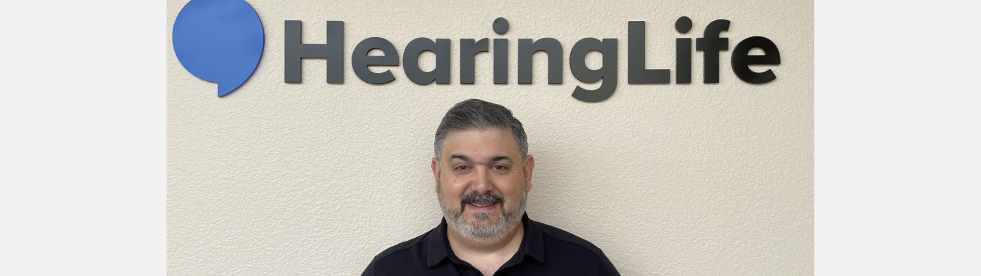 Tod Borges smiling in front of the HearingLife logo sign