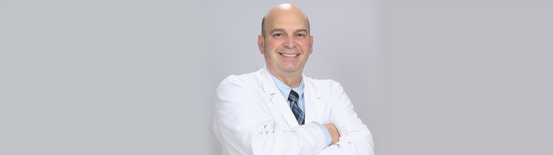 Professional wearing a white lab coat and a tie, smiling in a confident and welcoming manner.