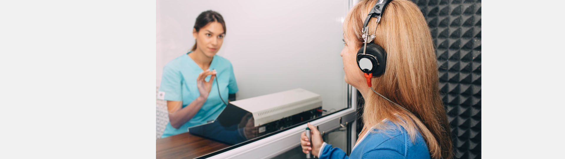 Professional hearing test conducted in a soundproof room, featuring an audiologist evaluating a patient wearing headphones.