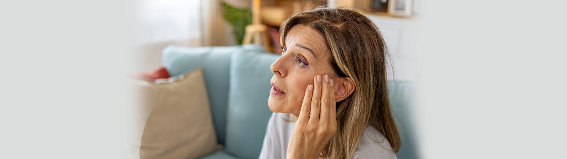 Woman seated on a sofa, touching her ear with a concerned expression.