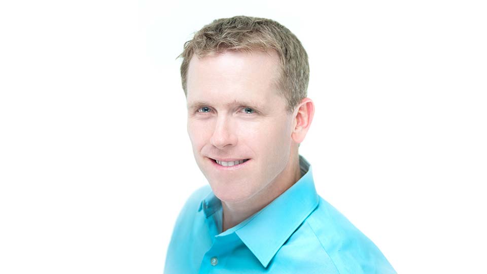 Hearing care expert wearing a light blue collared shirt against a white background.