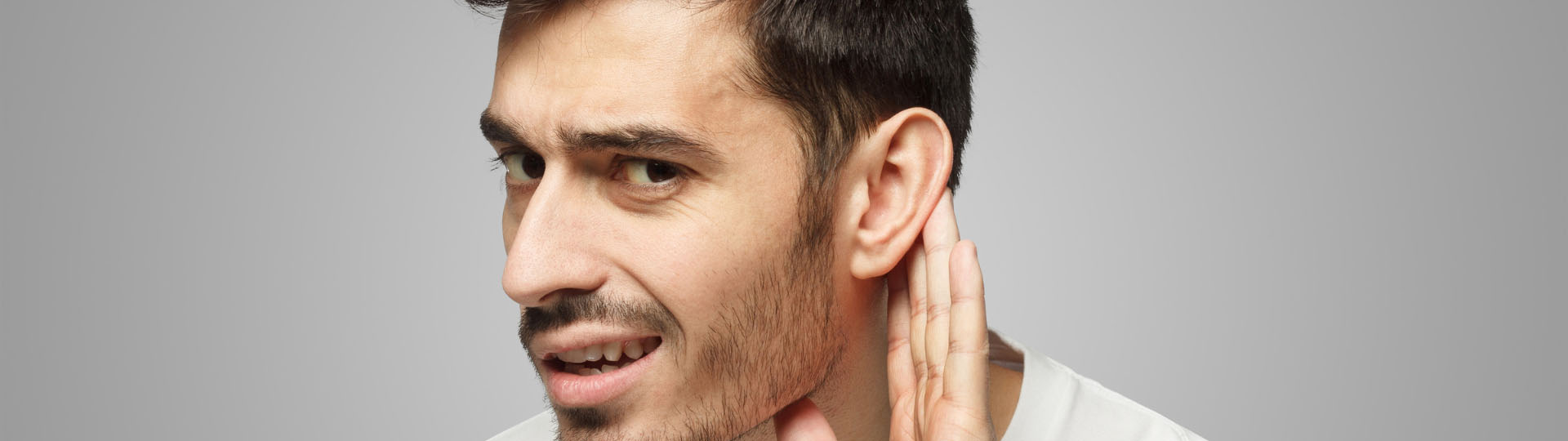 man cupping hand to ear with a concerned expression, suggesting difficulty hearing or sudden hearing loss