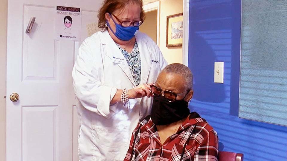 Hearing care specialist adjusting a hearing aid for a patient in a brightly lit clinic.