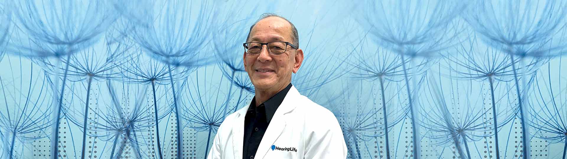 Tim Lin, hearing care professional wearing a white coat, standing in front of a blue dandelion-inspired background.