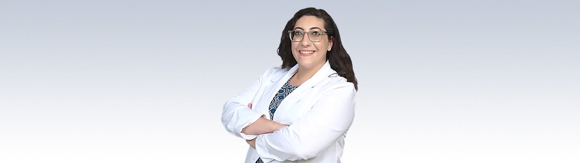 Dr. Eleni Santarelli, Audiologist at HearingLife, wearing a white coat with arms crossed against a gradient background.