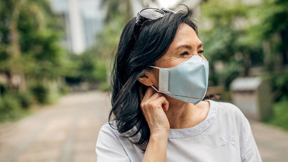 woman adjusting hearing aid while wearing a face mask outdoors