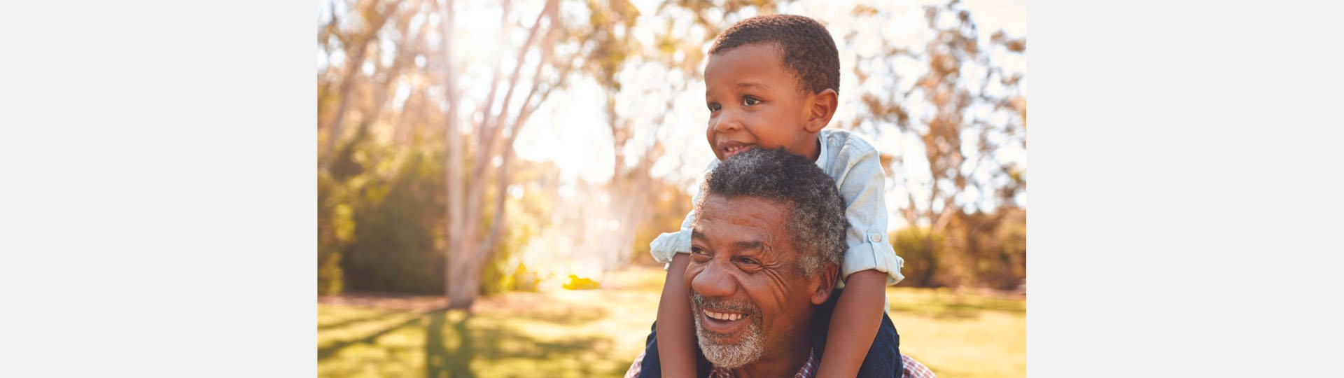 father carrying child on his shoulders in a sunny park setting surrounded by trees