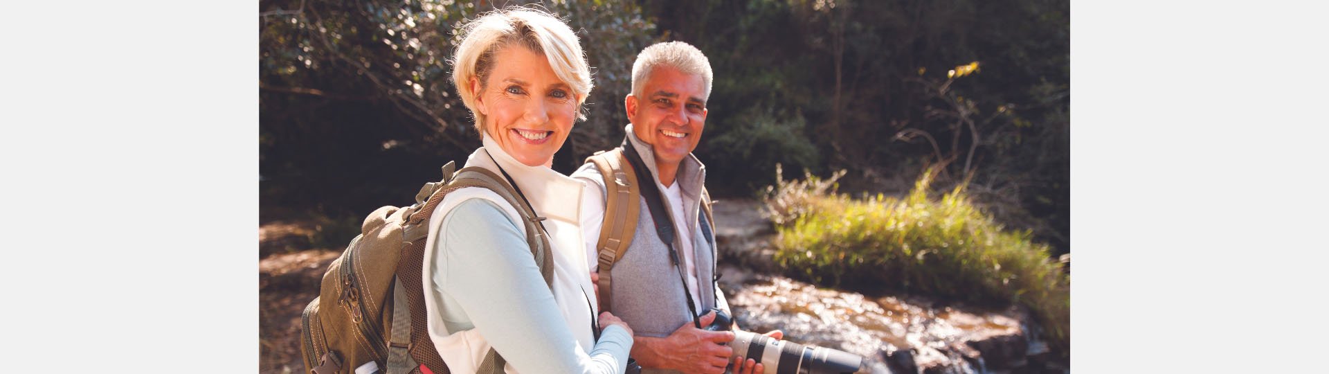 couple enjoying a hike with hearing aids, carrying backpacks and a camera near a forest stream