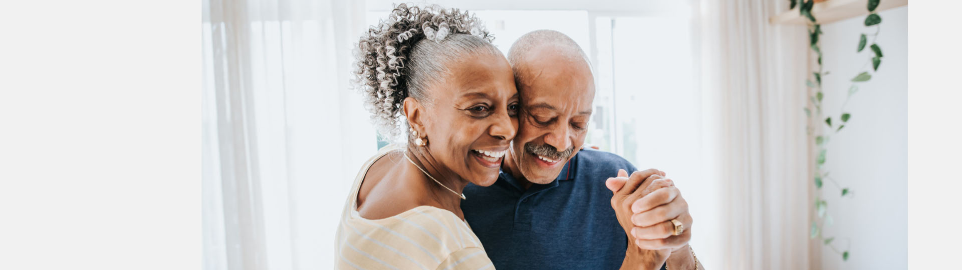 Senior couple holding hands while dancing in a bright living room.
