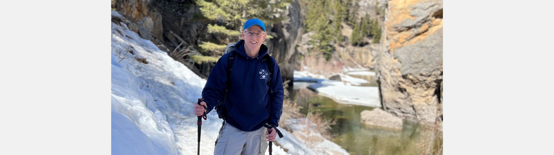 audiologist Jeff Williamson hiking on a snowy trail in Montana by a river and rocky cliffs