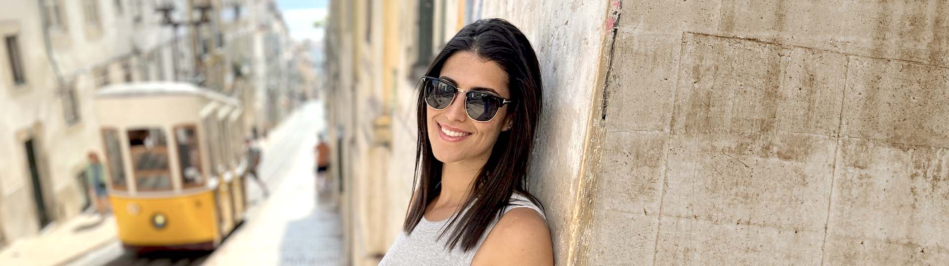 woman leaning against a wall on a sunny street with a yellow tram in the background