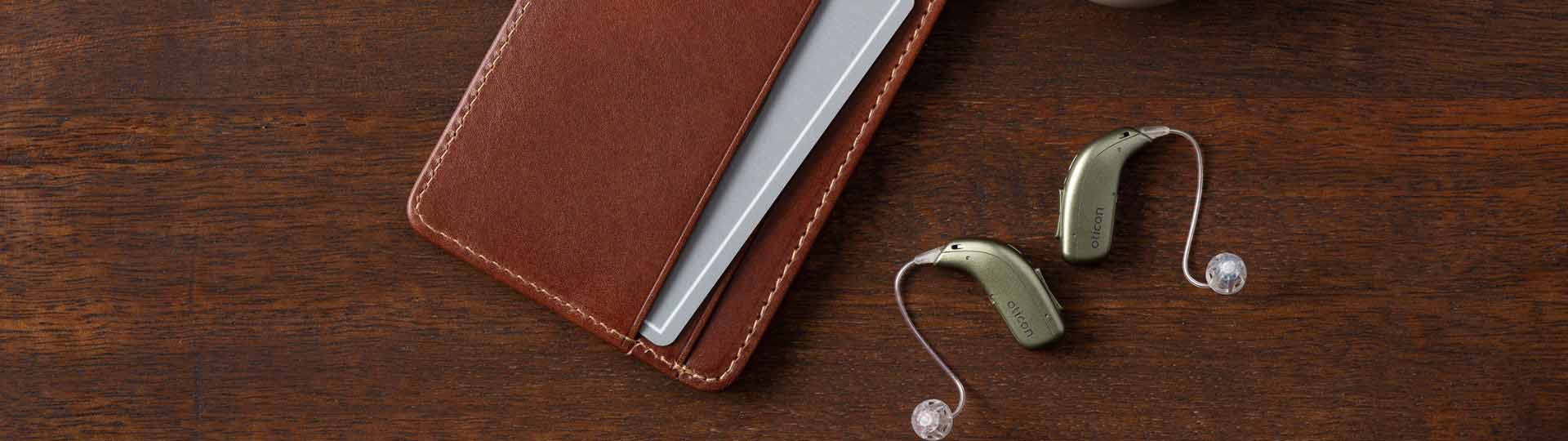 hearing aids paired with a leather wallet on a dark wooden surface
