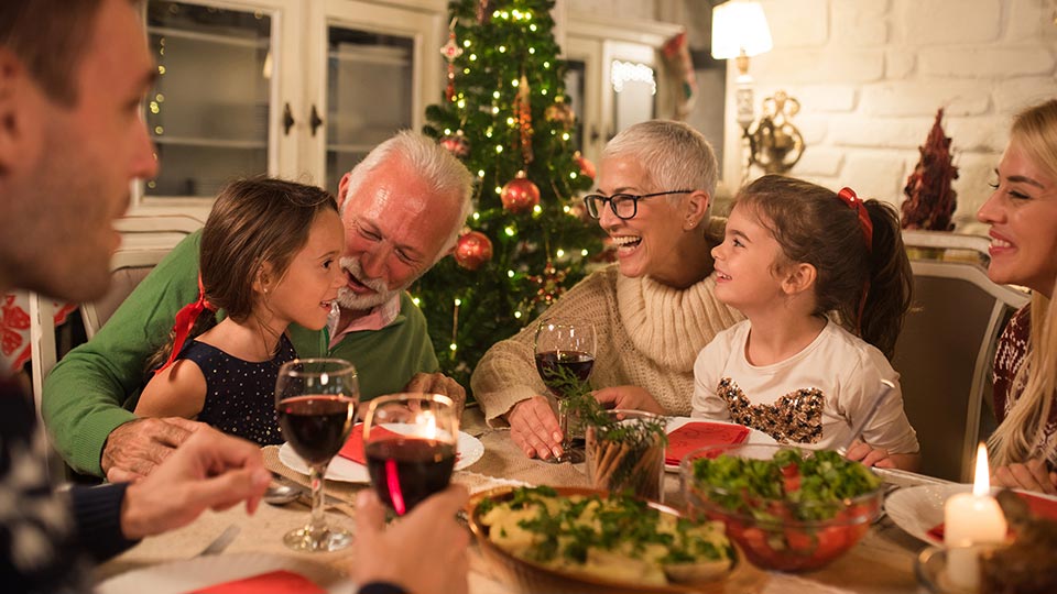 Festive dinner table with family members sharing a holiday meal near a decorated Christmas tree.