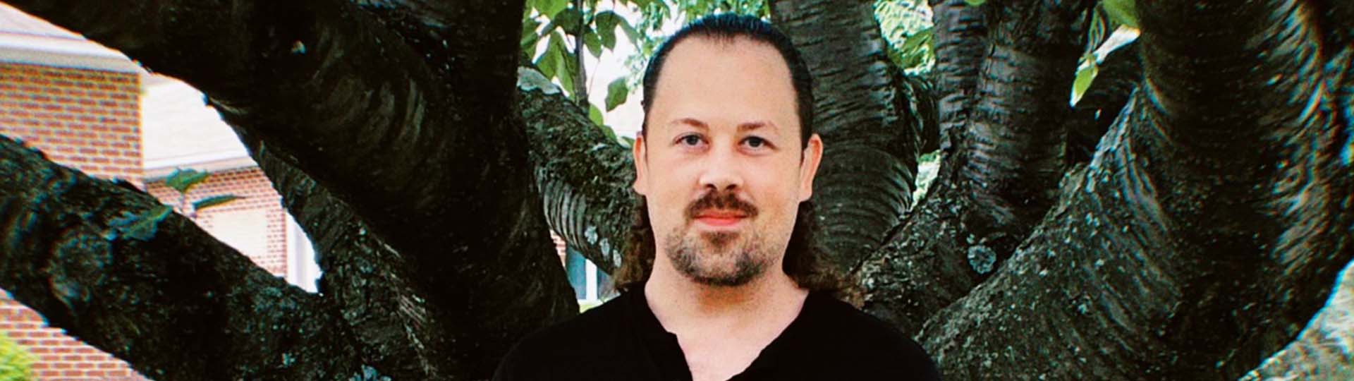 Walter standing outdoors near a large tree with thick branches in a residential area.