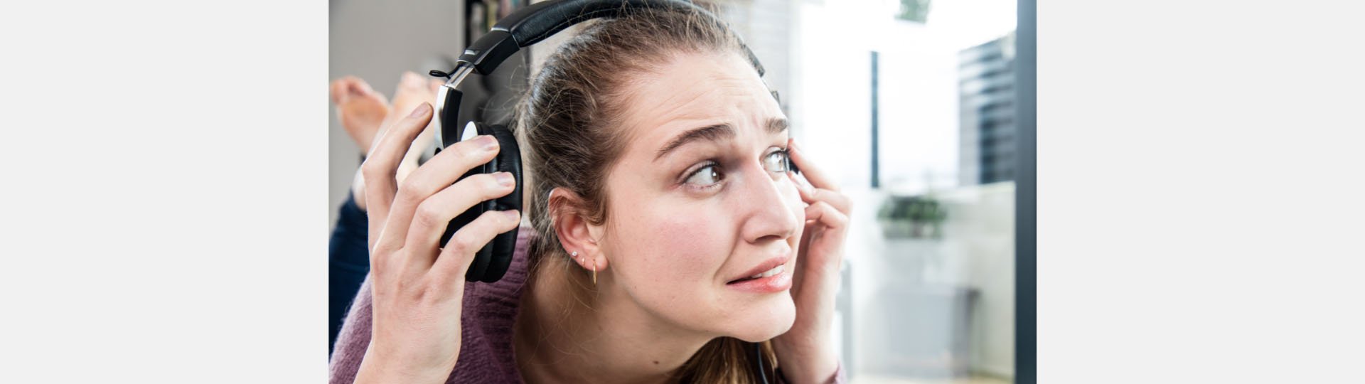 Woman holding headphones, appearing uncomfortable due to loud sound.