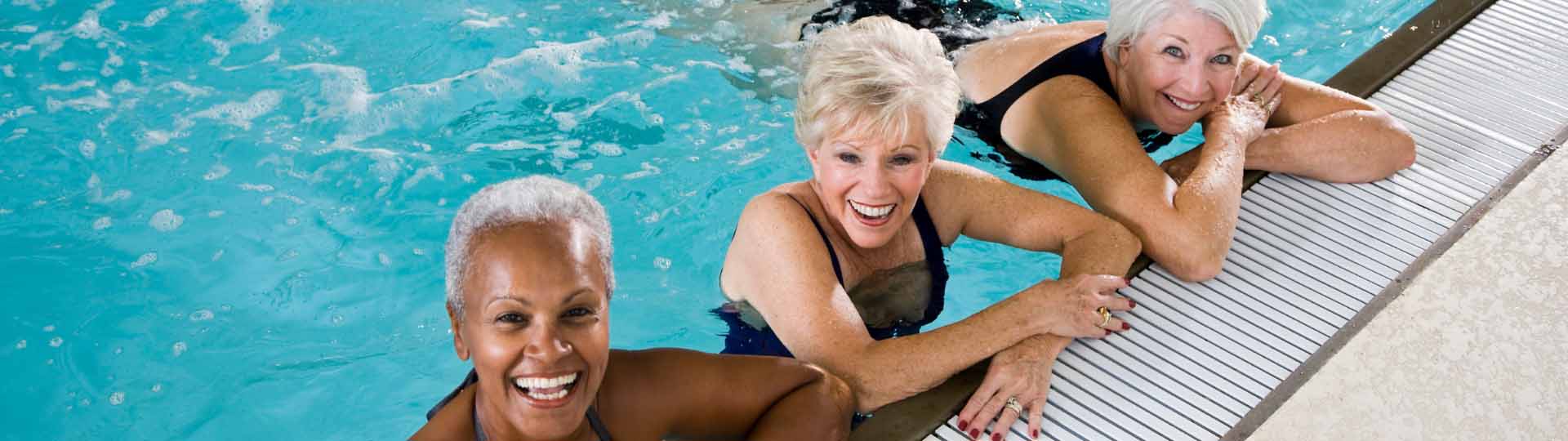 Three women relaxing and smiling in a swimming pool by the edge.