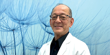 Hearing care professional wearing a white coat, standing against a blue background featuring dandelion artwork.