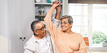 Two older adults joyfully dancing together in a bright kitchen, highlighting happiness and active lifestyles.