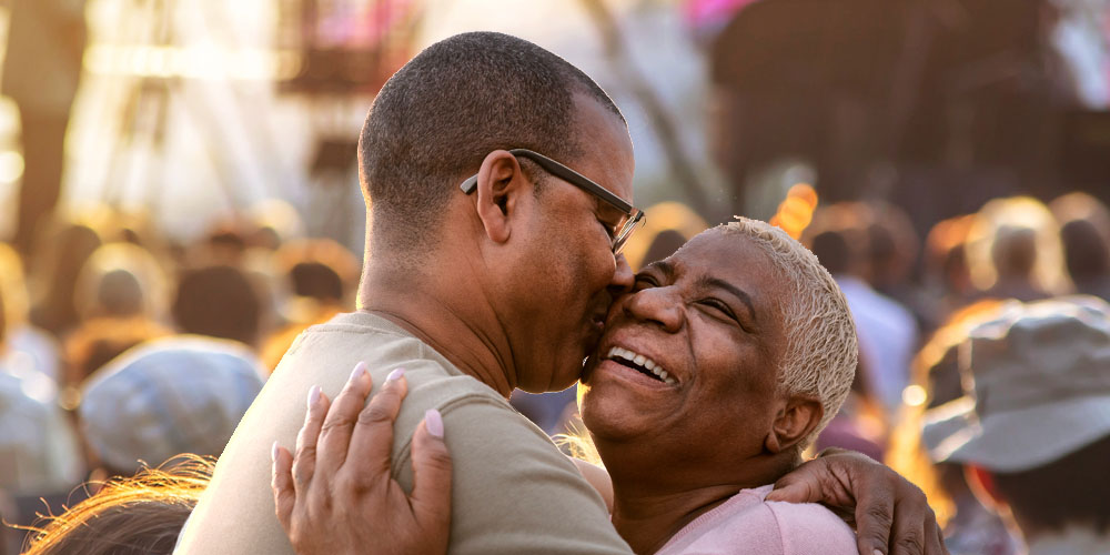 Man with a hearing aid embracing a woman while dancing at a lively outdoor concert.