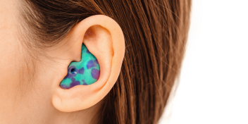 brightly colored custom earplug with a turquoise and purple pattern fitted in an ear