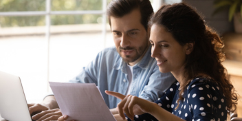 couple reading and discussing a document with a laptop on a table