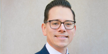 Professional audiologist wearing formal attire and glasses.