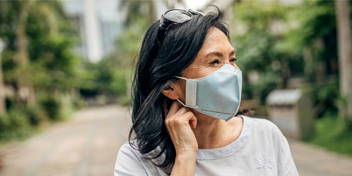 woman wearing a face mask outdoors while adjusting her hearing aid