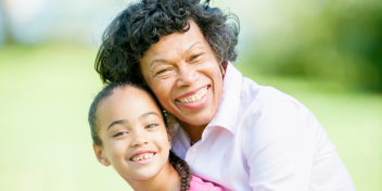 woman smiling and hugging a child in a sunny, green park