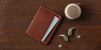 hearing aids placed near a brown leather wallet and beige portable speaker on a polished dark wooden surface
