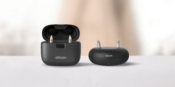 Oticon Real hearing aids in modern black chargers resting on a table