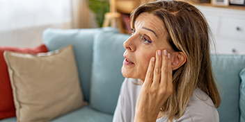 woman adjusting her hearing aid while sitting on a couch