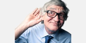 older man in glasses cupping his ear, demonstrating hearing difficulty