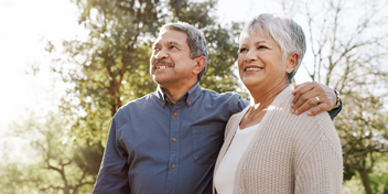 older couple smiling outdoors on a sunny day, promoting awareness of hearing health