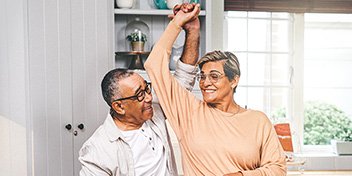 Two older adults joyfully dancing together in a bright kitchen.