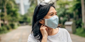 woman adjusting hearing aid while wearing a face mask outdoors