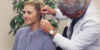 Hearing specialist examining a patient's ear with an otoscope in a clinic setting