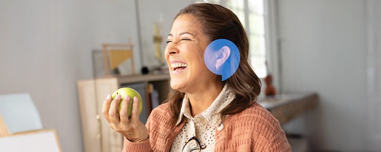 Woman smiling joyfully with a HearingLife speechbubble icon over her ear