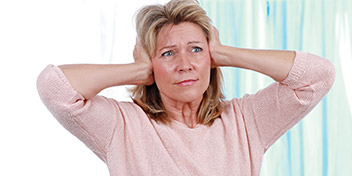 Woman experiencing discomfort while covering her ears with both hands.