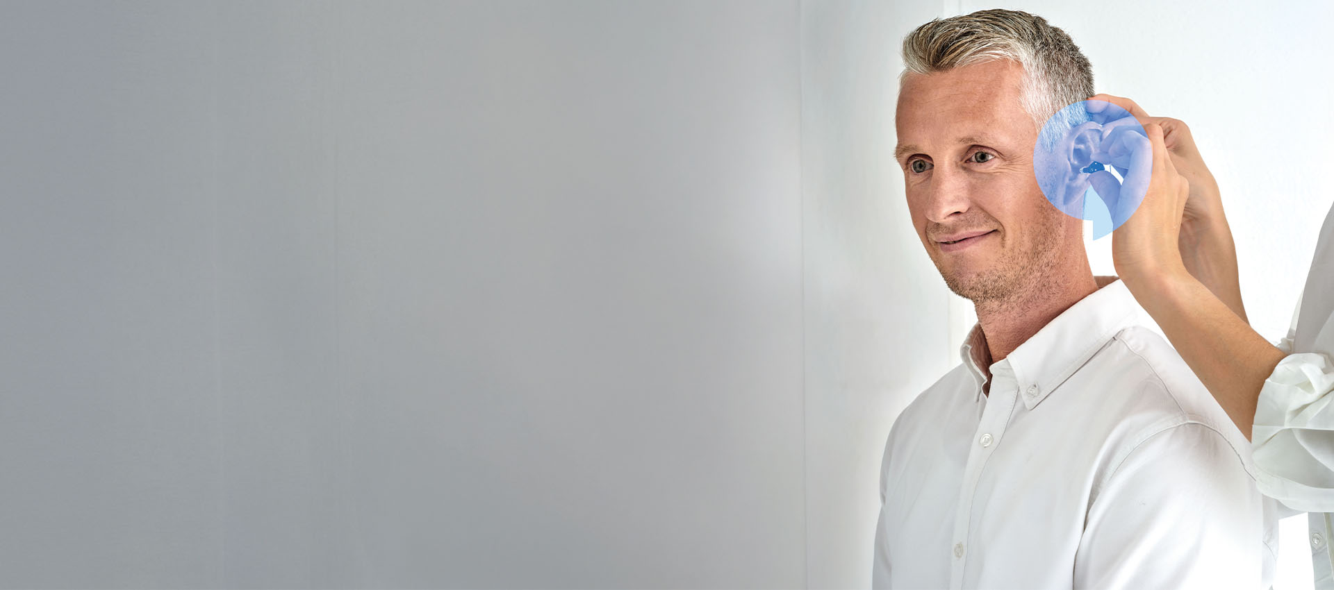 Man smiling while a hearing care professional fits a hearing aid.