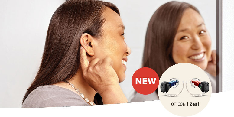 New Oticon Zeal™ --- woman smiling and pointing at her ear to show how discreet the hearing aid is