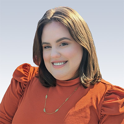 allison phillips wearing an orange blouse with a gold necklace against a light blue background
