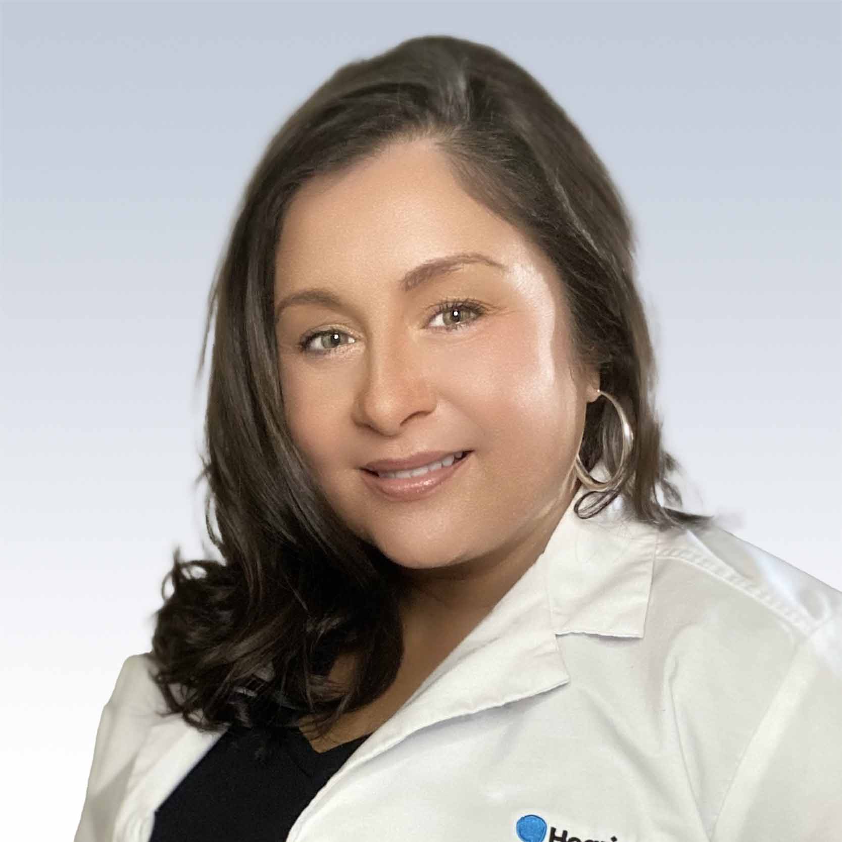 angela ricker, hearing care professional at HearWell Clinics, wearing a white lab coat against a light gradient background