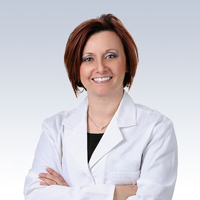 Hearing care professional Anita Slate in a white lab coat with arms crossed.