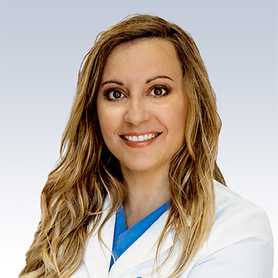 Ashley Genke, hearing care professional wearing a white coat and blue scrubs, representing expertise in audiology services.