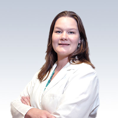 Brandy Gliniecki, hearing care professional wearing a white coat, standing confidently against a gradient background.