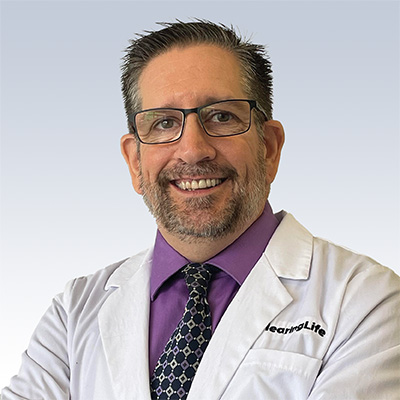 Hearing care specialist wearing a white lab coat with the HearingLife logo and a purple shirt.