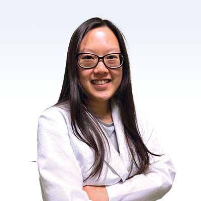 Hearing care professional in a white coat with long dark hair standing confidently.