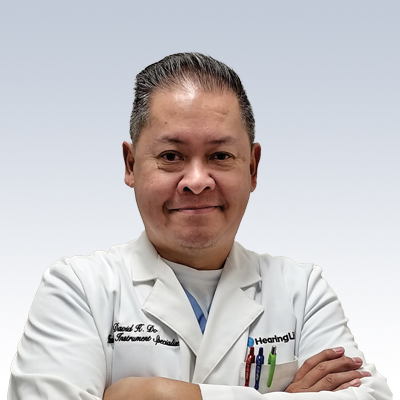 Hearing care professional David Do wearing a white lab coat with arms crossed.