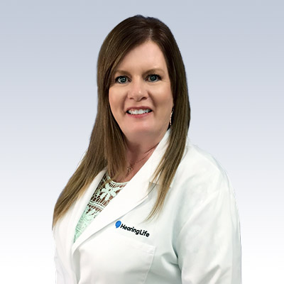 Deborah Young wearing a white coat with the HearingLife logo.